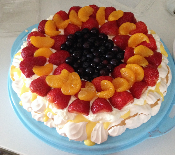 Ferdig pynta pavlova kake på fat med frukt, bær og vaniljekrem