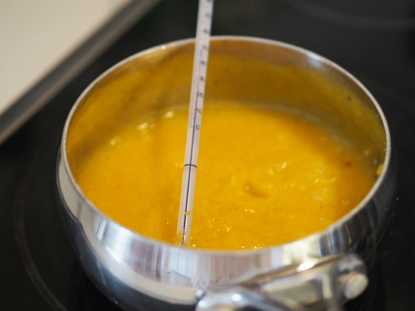 Bilde av en kjele med lemoncurd som kokes opp til riktig temperatur. Temperaturmål i kjelen. Bilde av en kjele med lemoncurd som kokes opp til riktig temperatur. Temperaturmål i kjelen.