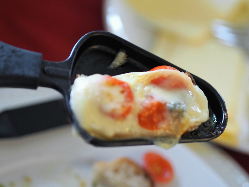 bilde av en skuff til raclette, et sosialt måltid. Den er fylt med tomat og ost
