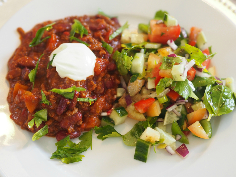 Bilde av chili con carne på tallerken, servert med rømme og salat
