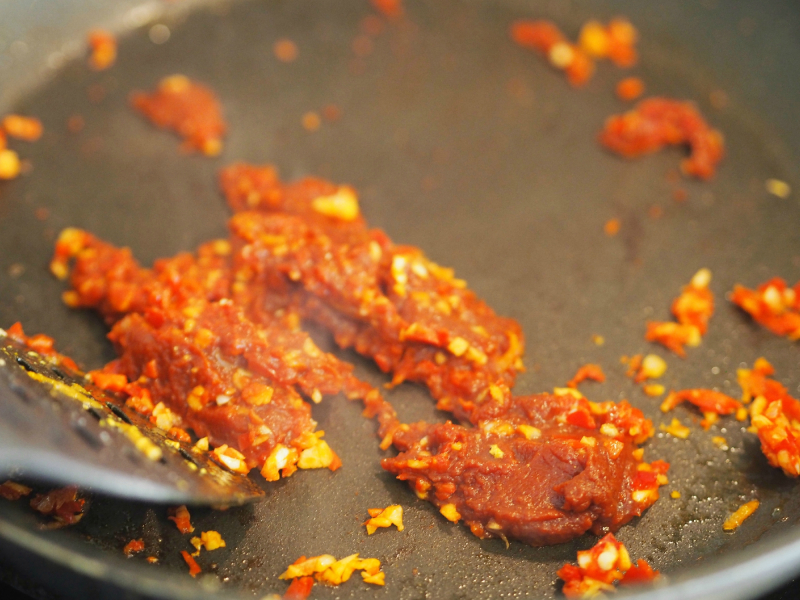 bilde av tomatpure, chili og hvitløk som stekes på panna. Masse gode smaker.